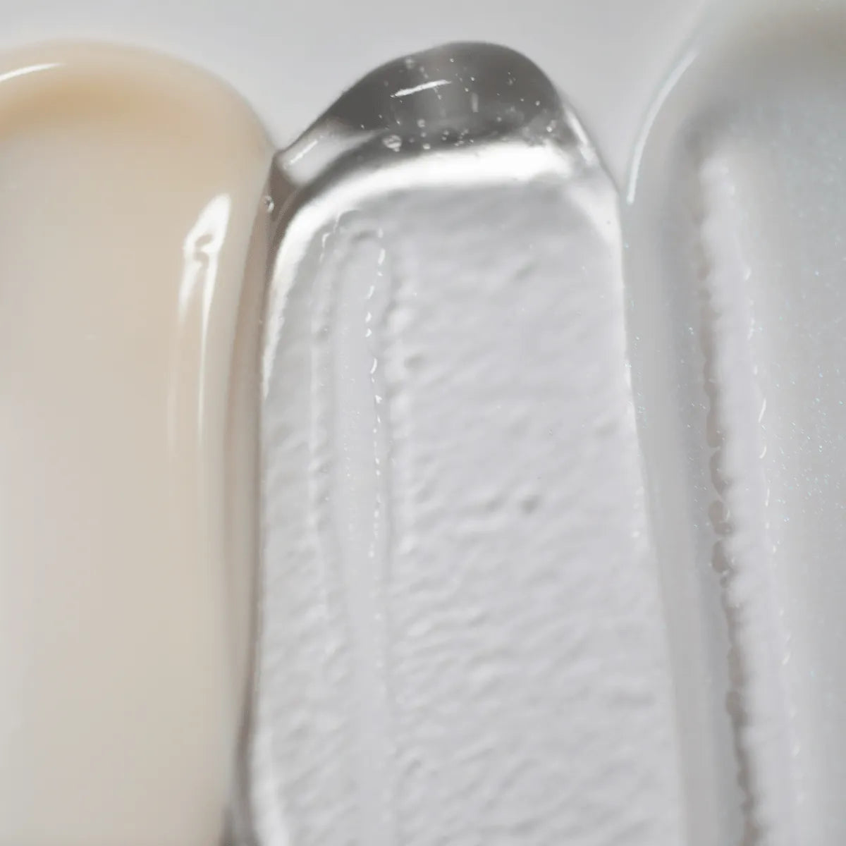 Un gros plan montre les textures du sérum activateur LightBoost Wand de Solawaves : beige crémeux, gel transparent infusé de la technologie LightBoost et crème lisse gris clair/blanc. Les textures varient de crémeuse à gélifiée, chacune présentant un fini brillant.